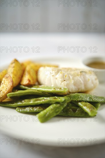 A tender fish fillet alongside fresh green beans and golden roasted potatoes. A small bowl of sauce complements the meal, creating an appetizing presentation