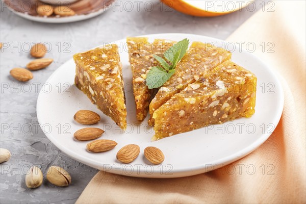 Traditional turkish candy cezerye made from caramelised melon, roasted walnuts, hazelnuts, cashew, pistachios on white ceramic plate and a cup of coffee on a gray concrete background. side view, close up, selective focus