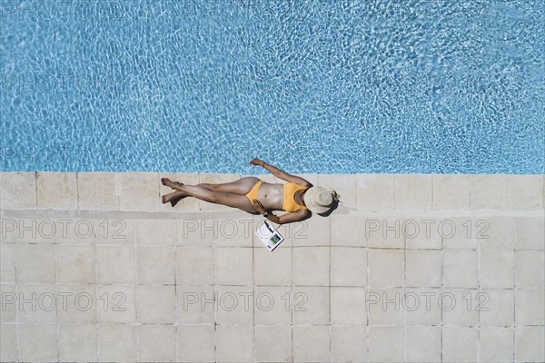 Young woman lying in the sun at the edge of a swimming pool, her face covered by a sun hat, Provence, France, Europe