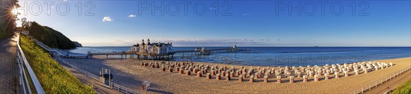 Sunlit beach with pier and historic building by the sea under a clear sky, Rügen, Sellin