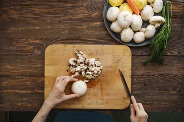 Unrecognizable woman chopping champignon mushrooms, top view