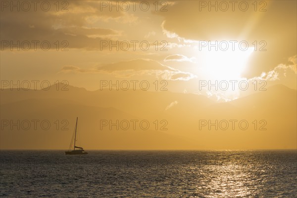 A sailboat on a calm sea at sunset with a golden sky and mountains in the background, Agia Kyriaki, Nafplio, Nauplia, Nauplion, Nafplion, Argolis, Argolic Gulf, Peloponnese