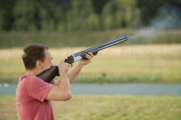 An old man shoots from a hunting rifle at a shooting range. Smoke from the barrel is visible in the frame