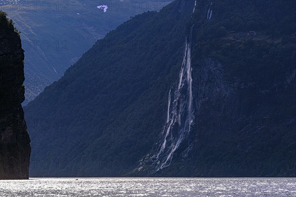 The Seven Sisters waterfall cascades along a steep cliff face into the Gairangerfjord, surrounded by mountains and nature in Norway Europe