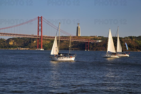 Two sailboats on calm waters with a red suspension bridge in the background under a blue sky, Lissabon, 25 de Abril Bridge