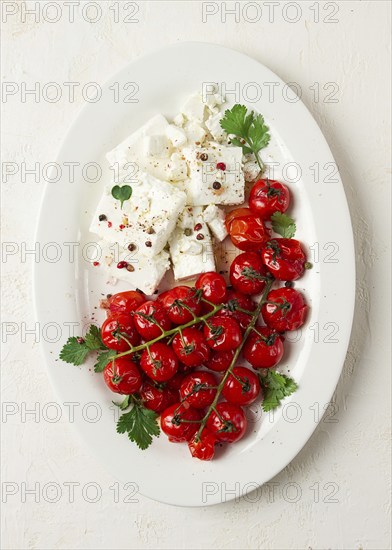 Baked cherry tomatoes, with cheese, and spices, on a white plate, homemade, no people