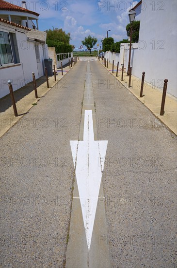 Narrow road with white arrow, flanked by buildings under a blue sky, Saintes-Maries-de-la-Mer, Camargue, France, Europe