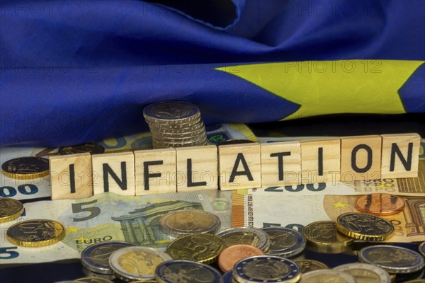 Symbolic image of inflation (in the euro area) : The word INFLATION in letter cubes on euro coins and banknotes