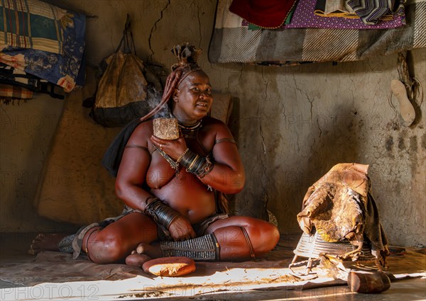 Traditional Himba woman caring for her body with smoke, interior of the first woman's mud hut in a Himba village, traditional ochre dye container and woven frame with leather for caring for the body with smoke at Opuwo near Opuwo, Kaokoveld, Kunene, Namibia, Africa