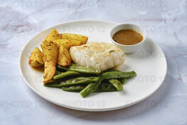 Tender baked cod is paired with vibrant green beans and crispy roasted potato wedges. A savory dipping sauce completes this well-balanced meal