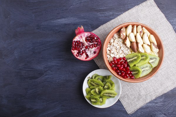 A plate with muesli, kiwi, pomegranate, Brazil nuts on a black wooden background. top view. copy space