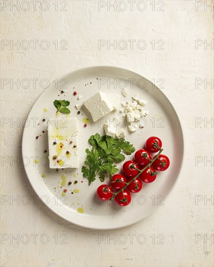 Feta cheese, for salads, with cherry, green butter, greens, on a white plate, appetizer, top view, close-up