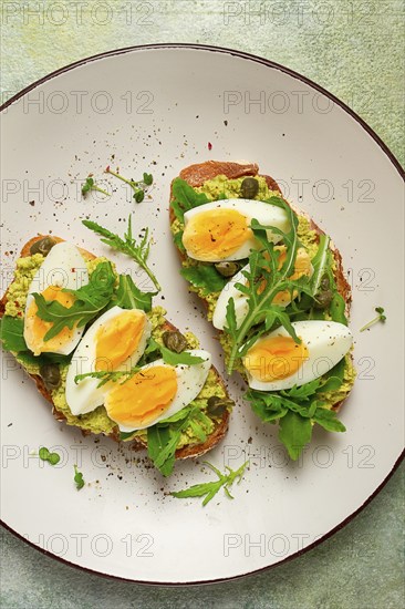 Sandwich with mashed avocado, boiled egg, and arugula, on bread, homemade, breakfast