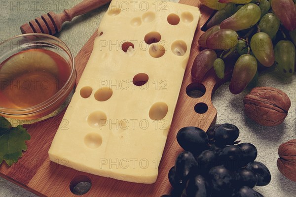 Cheese with big holes, emmental, maasdam, brie cheese, on a cutting board, with grapes and honey, nuts, appetizer to wine, top view