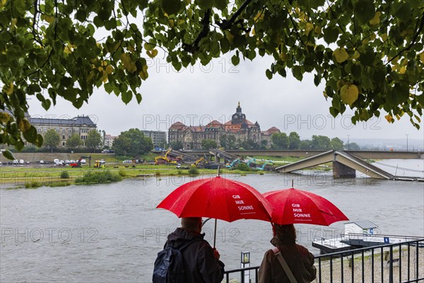 In the early hours of the morning, a section of the Carola Bridge collapsed for unknown reasons. Over a length of around 100 metres, the section on which the trams normally run has collapsed into the Elbe. Partial demolition has begun, with around 10 excavators tearing down the collapsed section of the bridge to make room for the impending Elbe flood. A pair of tourists with red umbrellas bearing the words Give me sunshine look out from Brühl's Terrace at the site of the accident, demolition of the Carola Bridge in Dresden, Dresden, Saxony, Germany, Europe