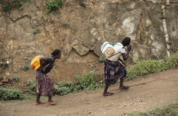 Two woman carry heavy water canisters on their backs from the water point to the village, near the village of Konso, southern Ethiopia