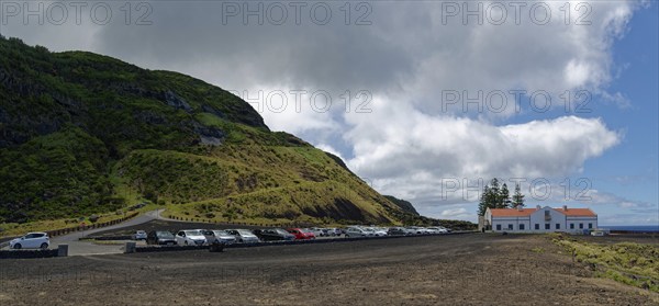 Car park with many cars next to a white house and thermal bath in a lava landscape under a cloudy sky, Termas da Ferraria, Sao Miguel Island, Azores, Portugal, Europe