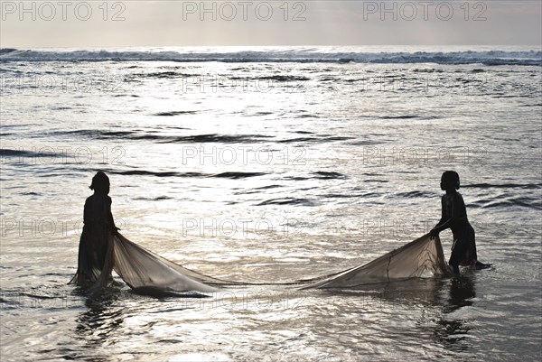 Silhouette of two girls fishing bichiques on the Indian ocean coast, Mananjary, Madagascar. Bichiques are fry of two species of freshwater fish belonging to the family gobiidae