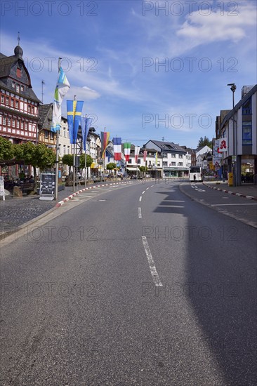 Main street with bus stop Adenau Markt, buildings, half-timbered houses, flags and trees under blue sky with cirrus clouds in Adenau, Eifel, Landkreis Ahrweiler, Rhineland-Palatinate, Germany, Europe