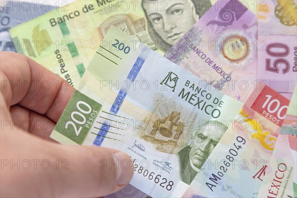 A person holding a two hundred Mexican Banknote with more bill on the background. Concept: Inflation