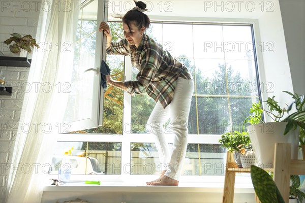 Woman manually washes the window of the house with a rag with spray cleaner and mop inside the interior with white curtains. Restoring order and cleanliness in the spring, cleaning servise