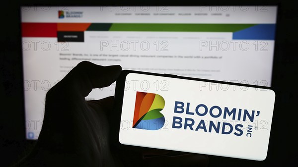 Stuttgart, Germany, 03-13-2024: Person holding smartphone with logo of US restaurant holding company Bloomin' Brands Inc. in front of website. Focus on phone display, Europe