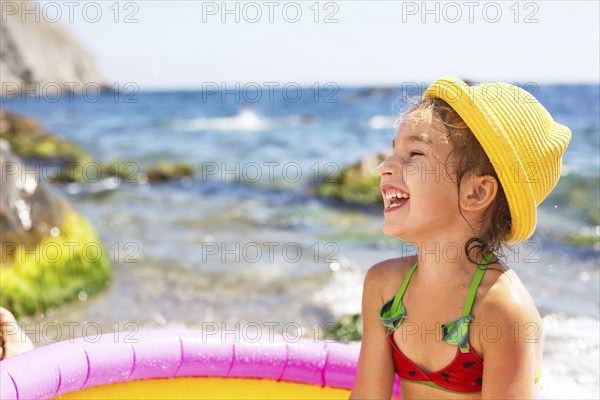 Girl in yellow straw hat plays in outdoor near sea, in water with a bucket in an inflatable pool on the beach. Indelible products to protect children's skin from the sun, sunburn. resort at the ocean