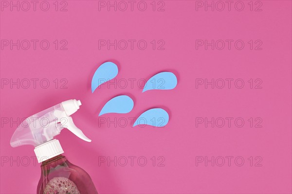 Cleaning agent spray bottle with blue liquid drops cut from paper on pink background