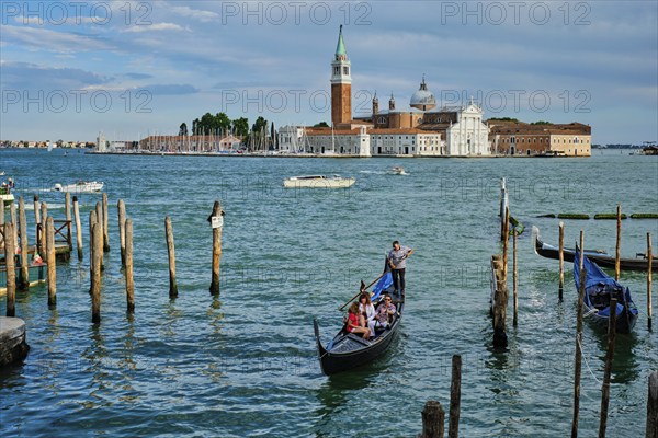 VENICE, ITALY, JUNE 27, 2018: Gondolier with tourists in gondola in lagoon of Venice by Saint Mark (San Marco) square with San Giorgio di Maggiore church in background in Venice, Italy, Europe