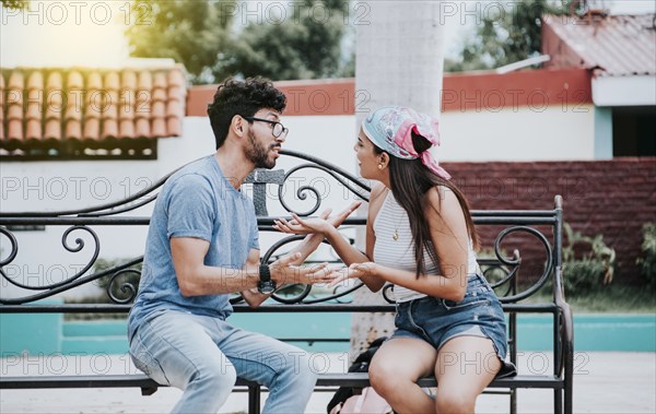 Man arguing with his girlfriend sitting in a park. Young couple arguing sitting on a park bench, Concept of aggressive couples in the park. Upset couple arguing on a park bench