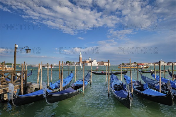 VENICE, ITALY, JUNE 27, 2018: Gondolas and gondolier in lagoon of Venice by Saint Mark (San Marco) square with San Giorgio di Maggiore church in background in Venice, Italy, Europe