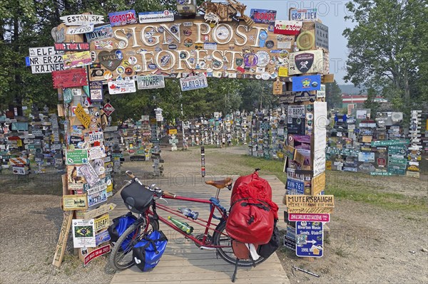 Bicycle with luggage in front of town and road signs in the signpost forest, cycling trip, cycling adventure, Watson Lake, Yukon Territory, Alaska Highway, Canada, North America