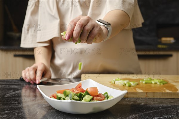 Closeup of hand of woman dropping a sliced celery stalk into a dish with salad