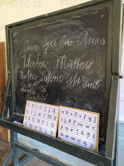 Old historical school board on it below Sütterlin alphabet upper case lower case letters above it in words written in Sütterlin Oma Opa Otto Anna Vater Mutter Unsere Lehrerin ist lieb dumm in old rebuilt school house and town hall from year 1830 in Freilichtmuseum Neuhausen, Neuhausen ob Eck, Kreis Tuttlingen, Baden-Württemberg, Germany, Europe