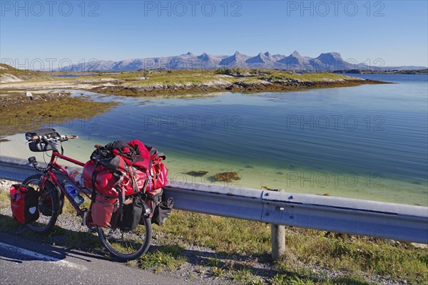 Packed touring bike, crystal clear water in a shallow bay, view of the mountain range Seven Sisters, cycle tourism, cycle trip, Heröy Island FV 17, Kystriksveien, Nordland, Norway, Europe