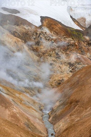 Steaming stream between colourful rhyolite mountains and snowfields, Hveradalir geothermal area, Kerlingarfjöll, Icelandic Highlands, Iceland, Europe