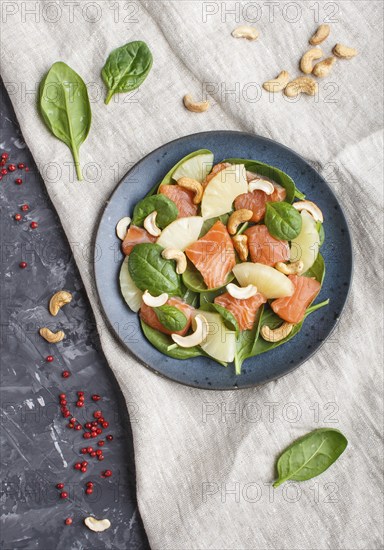 Fresh salmon with pineapple, spinach and cashew on a black concrete background. Top view, flat lay, linen tablecloth