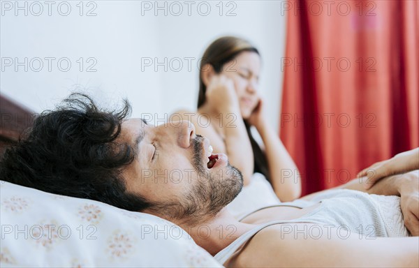 Snoring man in bedroom and wife covering her ears. Husband snoring while the wife suffers and covers her ears. Sleep apnea concept