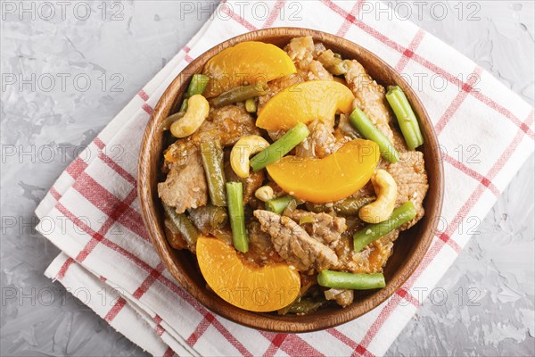 Fried pork with peaches, cashew and green beans in a wooden bowl on a gray concrete background. Top view, close up, chinese cuisine