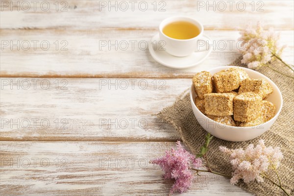 Traditional turkish delight (rahat lokum) in white ceramic plate with cup of green tea on a white wooden background. side view, copy space