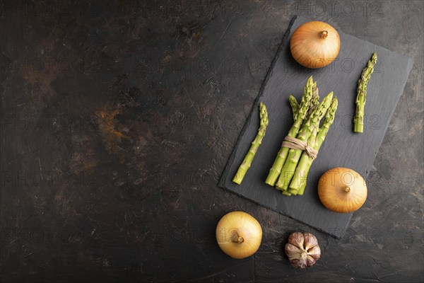 Bunch of fresh green asparagus, garlic, onion on slate board on black concrete background. Top view, flat lay, copy space. harvest, healthy, vegan food, concept