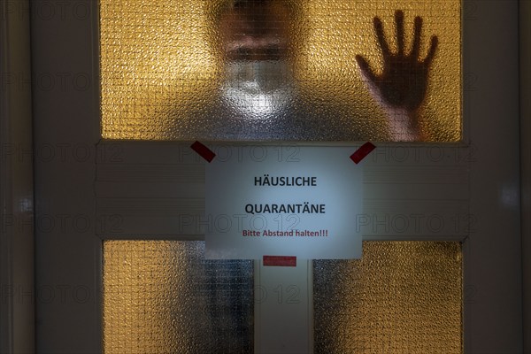 Symbolic image Domestic quarantine, man is in isolation at home due to a suspected corona infection, warning sign for visitors on the front door, communicating with a visitor through the door