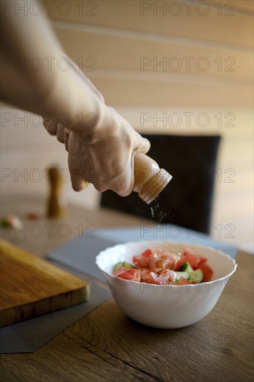 Close-up view of adding sea salt from a hand mill to a bowl with vegetable salad