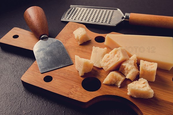 Hard cheese, parmesan, on a cutting board, cheese knife, grater, top view, no people