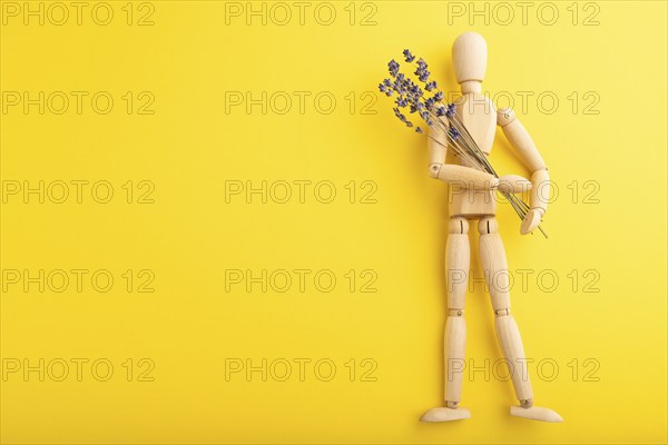 Wooden mannequin holding lavender flowers on yellow pastel background. copy space, isolated, summer, gardening concept