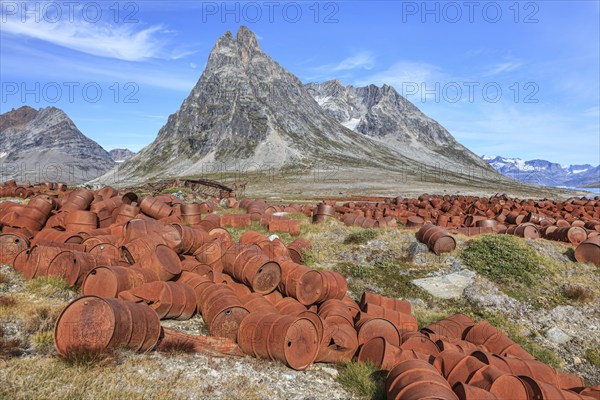 Rusted oil barrels on a fjord in front of steep mountains, remains of a US airbase from the Second World War, Ikateq Fjord, East Greenland, Greenland, North America