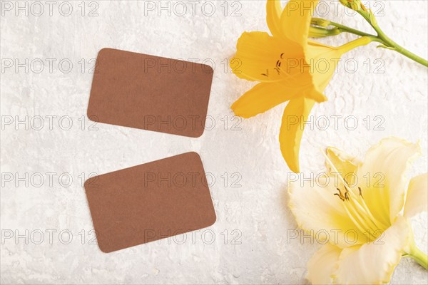 Brown paper business card mockup with orange day-lily flower on gray concrete background. Blank, top view, copy space, still life. spring concept