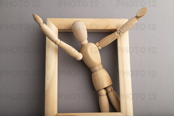 Wooden mannequin climbs out of a wooden frame with raised arms on gray pastel background. escape, break rules, freedom, welcome, greeting, joy concept