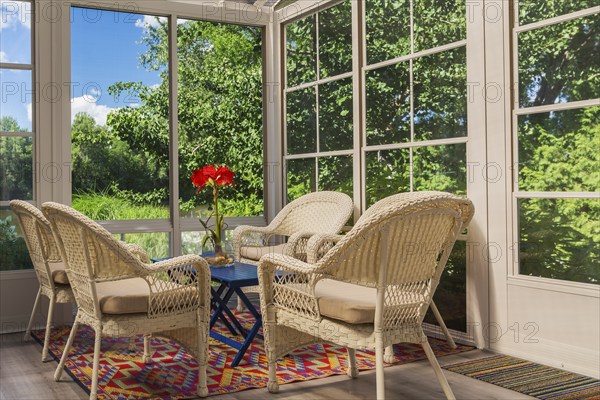 Beige wicker armchairs and blue wooden table in sunroom at back of luxurious residential home, Quebec, Canada, North America