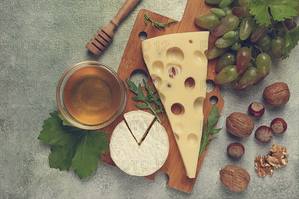 Cheese with big holes, emmental, maasdam, brie cheese, on a cutting board, with grapes and honey, nuts, appetizer to wine, top view